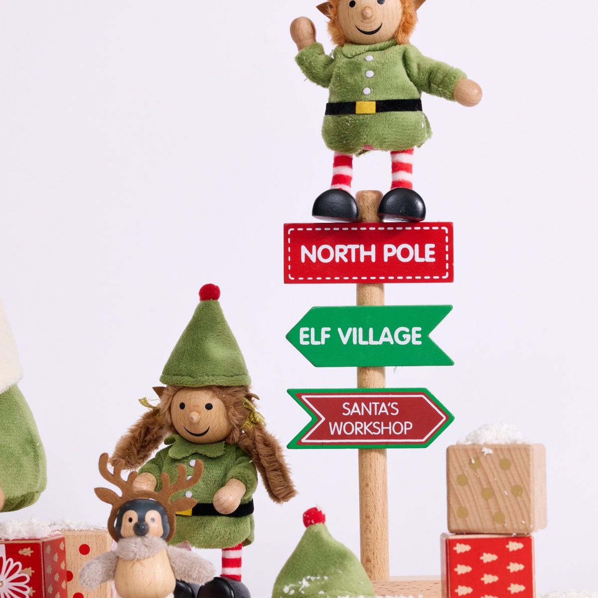 Cheeky Elves beside the North Pole signpost and wooden presents in a snowy Christmas scene
