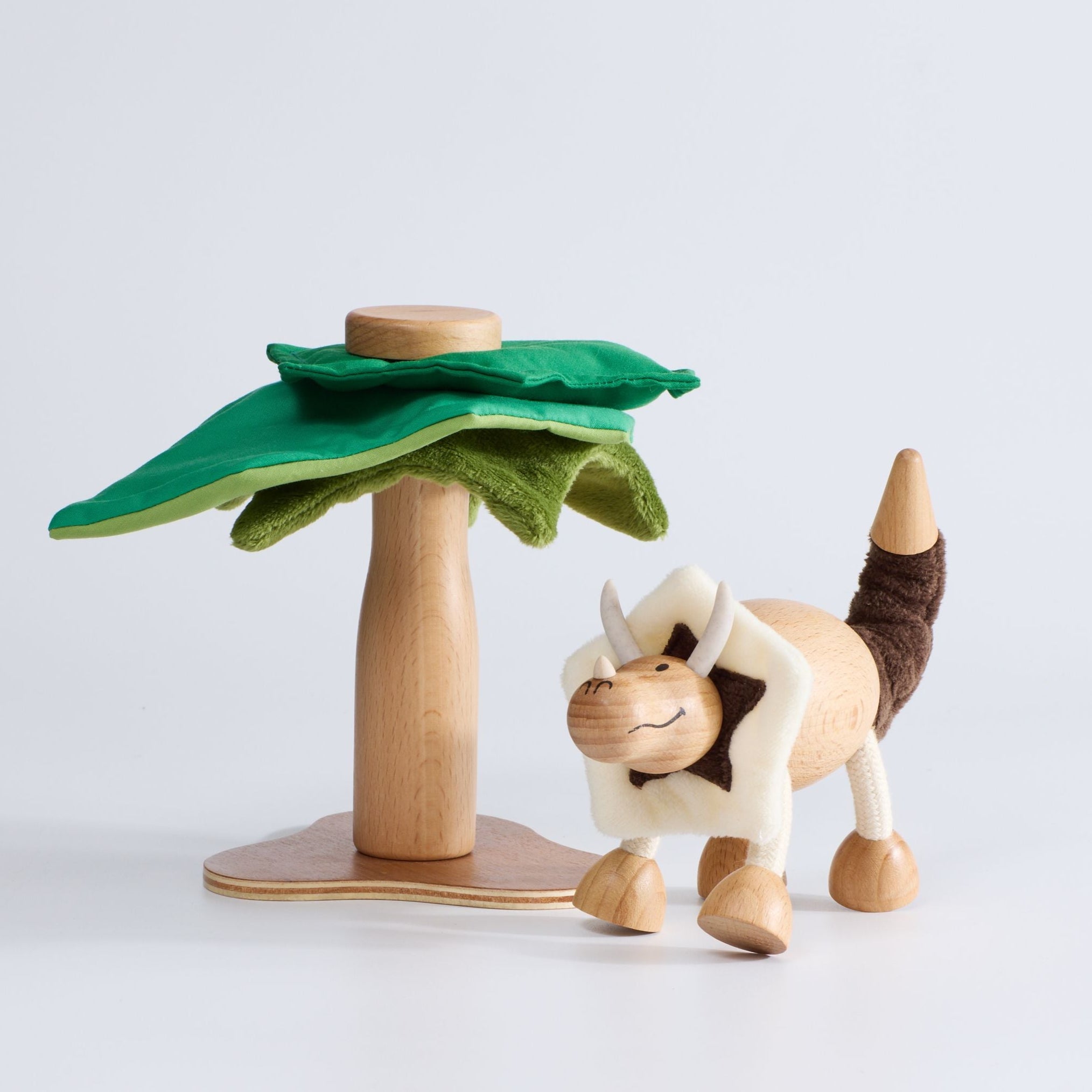 Wooden toy dinosaur with green felt tree on white background