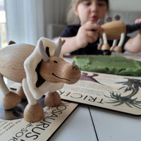 wooden dinosaur toy on a table with a small girl in the background playing another wooden dinosaur toy 