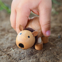 Small wooden wombat figurine held by a child's hand on dirt background