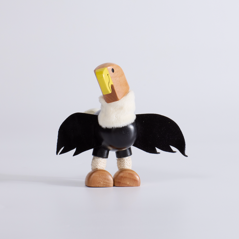 Wooden toy figure of a bird with black wings and a yellow beak on a light gray background