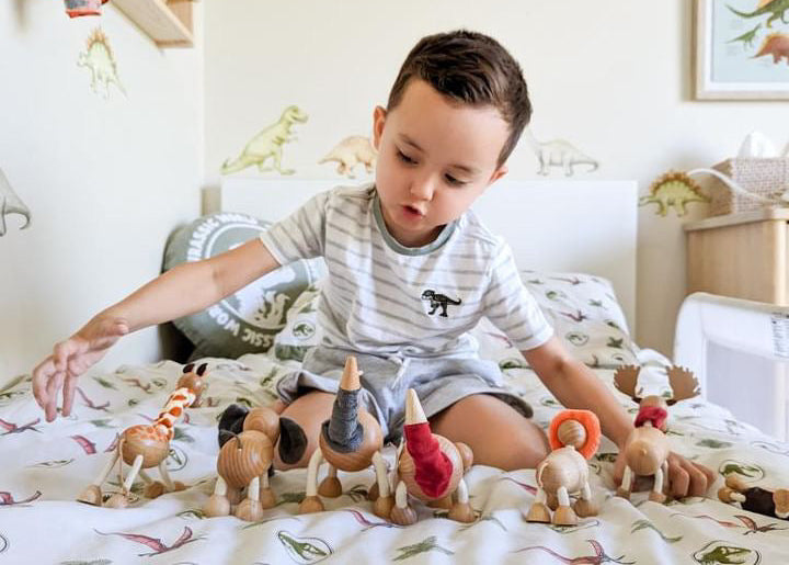 Child playing with Anamalz dinosaurs on a bed