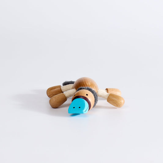 A plush toy platypus, with beige body, black tail, and blue accents on its face and feet.