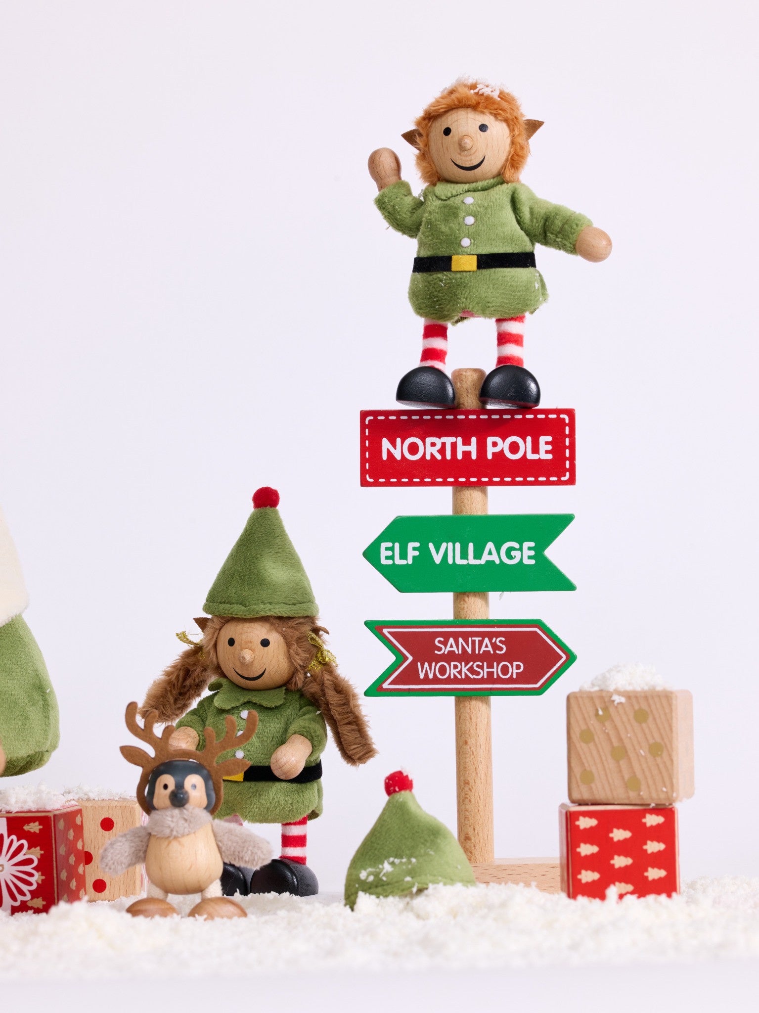 Cheeky Elves beside the North Pole signpost and wooden presents in a snowy Christmas scene